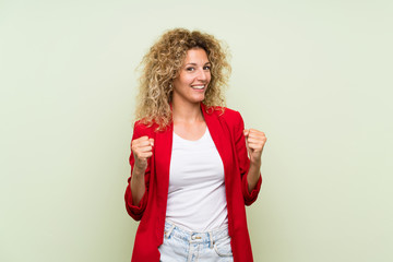 Young blonde woman with curly hair over isolated green background celebrating a victory in winner position