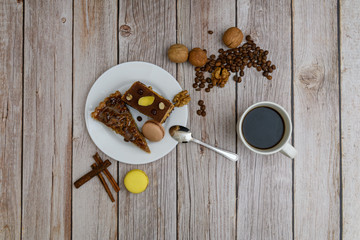 Cup of coffee and two slices of cake and macaroons on the plate on wooden table