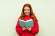 © luismolinero - Teenager redhead girl with sweater over isolated green background holding and reading a book