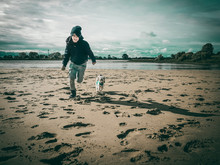 Boy Running With Dog At Beach Against Sky