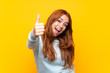 © luismolinero - Teenager redhead girl over isolated yellow background with thumbs up because something good has happened