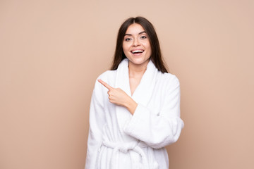 Wall Mural - Young girl in a bathrobe over isolated background pointing finger to the side