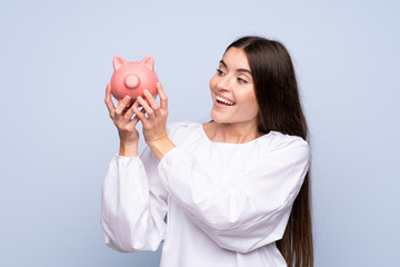 Wall Mural - Young woman over isolated blue background holding a big piggybank