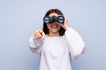 Wall Mural - Young woman over isolated blue background with black binoculars