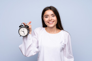 Wall Mural - Young woman over isolated blue background holding vintage alarm clock