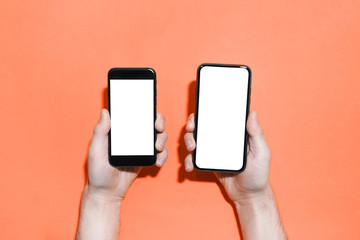 Close-up of two smartphones with mockup in male hands on background of lush lava color.