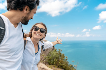 Wall Mural - Happy beautiful young couple of travelers man and woman take selfie on top of a mountain with ocean view. Romantic travels, honeymoon