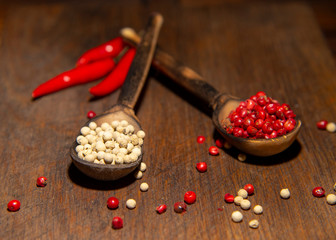 Two wooden spoons with red and white pepper on a wooden surface.