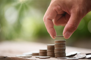 Hand putting coin on coin stack growing graph with green bokeh background,investment concept,Business Finance and Saving Money concept