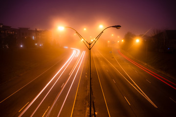 Colorful light traces of busy night traffic on highway. Atlanta city street, foggy autumn weather, GA, USA