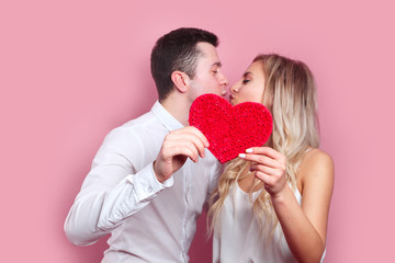 young couple kissing behind paper heart on pink background