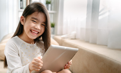 asian little girl playing with smartphone, technology and communication concept - smiling girl texting on smartphone and lying in bed at home