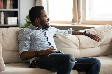 Relaxed african guy chill on sofa at home holding phone