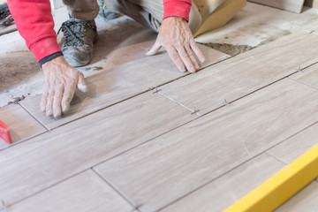 Man installing rectangular shaped floor tiles in kitchen. Applying adhesive before installation and verifying afterwards