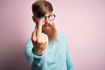 Canvas Print - Handsome Irish redhead man with beard wearing glasses over pink isolated background Showing middle finger, impolite and rude fuck off expression