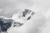 Atmospheric minimalist alpine landscape with massive hanging glacier on snowy mountain peak. Big balcony serac on glacial edge. Low clouds among snowbound mountains. Majestic scenery on high altitude.
