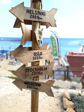 Wooden Route Pointer Showing Way To The Different Cities Of The World. Wooden Signpost To Moscow, Stockholm, Oslo, Helsinki Given In Kilometers.