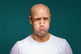 Fototapeta  - portrait of a bald man puffed out his cheeks on a blue background