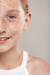 Wall Mural - Inclusive Beauty. Girl with freckles standing isolated on grey half face close-up smiling happy