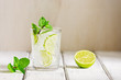 Refreshing cold drink with lime and mint in a glass on a white wooden board table. Traditional summer mojito cocktail. Selective focus, copy space.