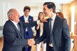 © Krakenimages.com - Group of business workers smiling happy and confident. Two of them, standing with smile on face shaking hands for agreement. Partners applauding at the office.