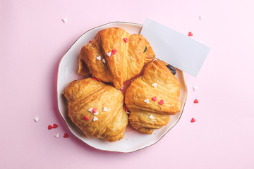 Valentine's day concept with two cups of coffee, almond croissant on pink plate on pink background. Top view,copy space. Romantic holiday. With empty card for your text