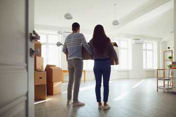 Rear view moving. Young couple family with boxes to move in a new house room.