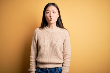 Sticker - Young beautiful asian woman wearing casual sweater over yellow isolated background making fish face with lips, crazy and comical gesture. Funny expression.