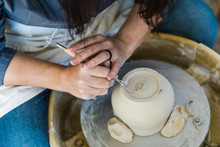 A Caucasian Woman Trimming The Base Of An Unfinished Clay Pot On A Pottery Wheel Close Up And Adding Detail Work To The Bottom