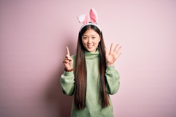 Sticker - Young asian woman wearing cute easter bunny ears over pink background showing and pointing up with fingers number six while smiling confident and happy.