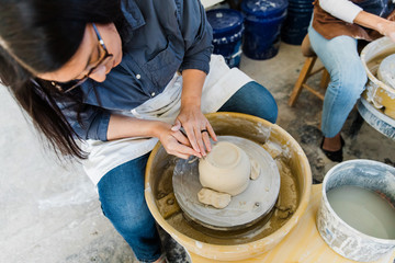 ceramic artist working at a pottery wheel in an art studio trimming clay pots