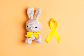 Wall Mural - Childhood Cancer Awareness Golden Ribbon with toy bunny on yellow background.