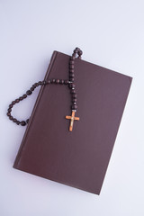 Wall Mural - A wooden cross with a rosary on a closed Holy Bible. Closed book with a brown cover and a symbol of christians on white background.