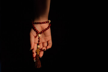 Wall Mural - Female hand wearing rosary. Black background. Religious prayer.