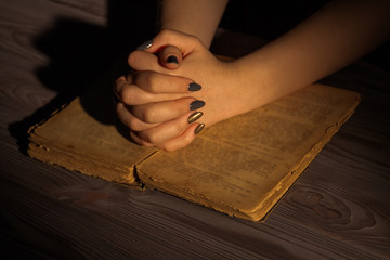 Wall Mural - Female hands with folded hands on holy bible. Woman's asking God in a dark room with very old opened ancient book.