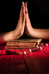 Wall Mural - Pair of hands pressed clasped together praying to God or Jesus. Close-up female hands with bible and rosary on black background.