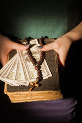 Rich christian, wealth and money concept. Female hands hold holy bible, money and rosary bead necklace.