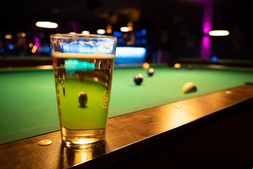 in a billiard parlor on the rail of a pool table is a glass with a beer