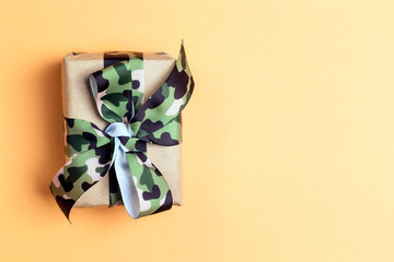 Wall Mural - Gift box with khaki ribbon on the yellow background. Defender of the Fatherland Day, February 23.