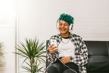 Woman At Home With Mobile Phone And Headphones On The Couch Sitting Listening To Music