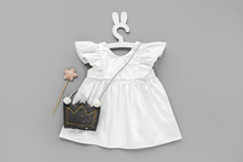 White Dress With Kids Handbag Shape Of Crown On Cute Hanger With Bunny Ears. Set Of  Baby Clothes And Accessories For Spring Or Summer On Gray Background. Fashion Childs Outfit. Flat Lay, Top View