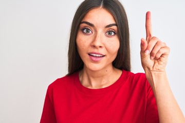 Wall Mural - Young beautiful woman wearing red casual t-shirt standing over isolated white background surprised with an idea or question pointing finger with happy face, number one