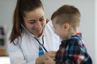 © H_Ko - Portrait of professional pediatrician listening to action of kids heart or breathing. Doc examining sick boy. Little baby standing near smiling doctor. Medicine and healthcare concept