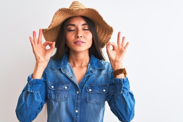 Wall Mural - Young beautiful woman wearing denim shirt and hat standing over isolated white background relax and smiling with eyes closed doing meditation gesture with fingers. Yoga concept.