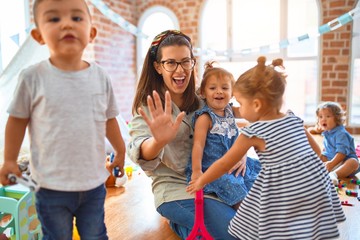 Wall Mural - Beautiful teacher and group of toddlers playing around lots of toys at kindergarten