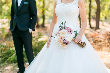 the bride in the white dress, the groom standing behind her and a bunch of flowers in her hand