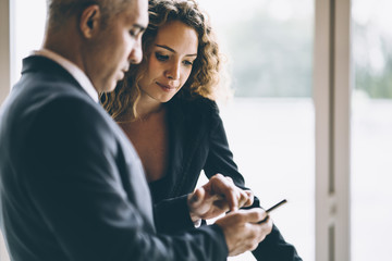 Scene of business woman looking at the cellphone of her colleague or her boss while the man point finger on his cell phone in the brightness meeting room atmosphere , concept business discussion.