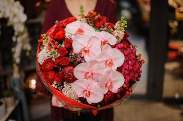 Woman holding a spring bouquet of red roses, peonies and hydrangeas with a pink orchid branch