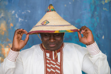 Handsome african man in traditional white dress and fulani hat looking down thinking, closeup portrait