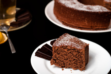 A piece of chocolate cake on a white plate on a black table